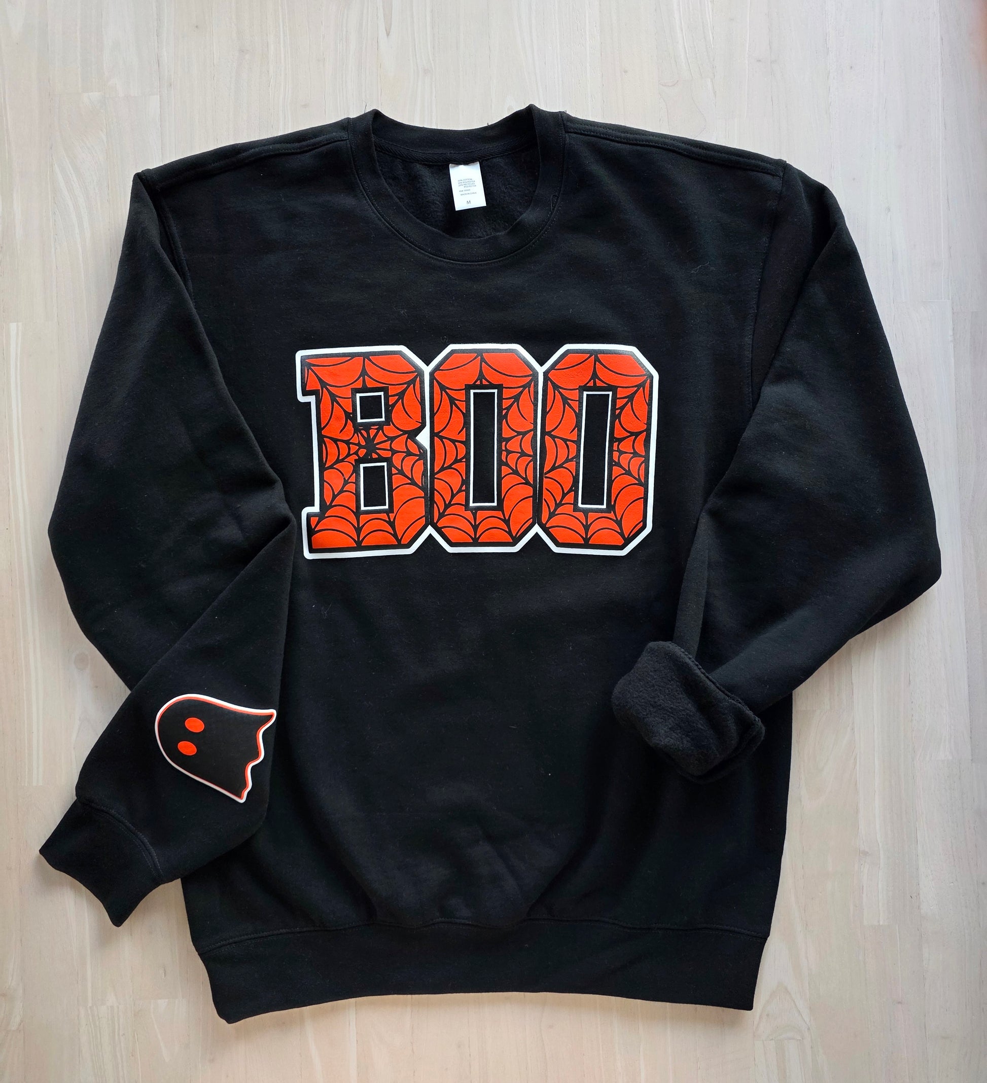 Black sweatshirt with 'BOO' design on a wooden surface