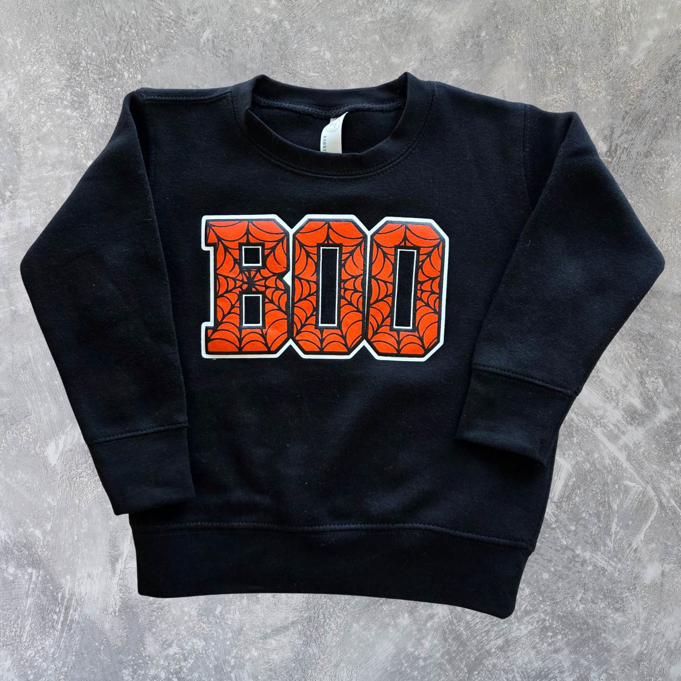 Black sweatshirt with orange 'BOO' text on a gray concrete background