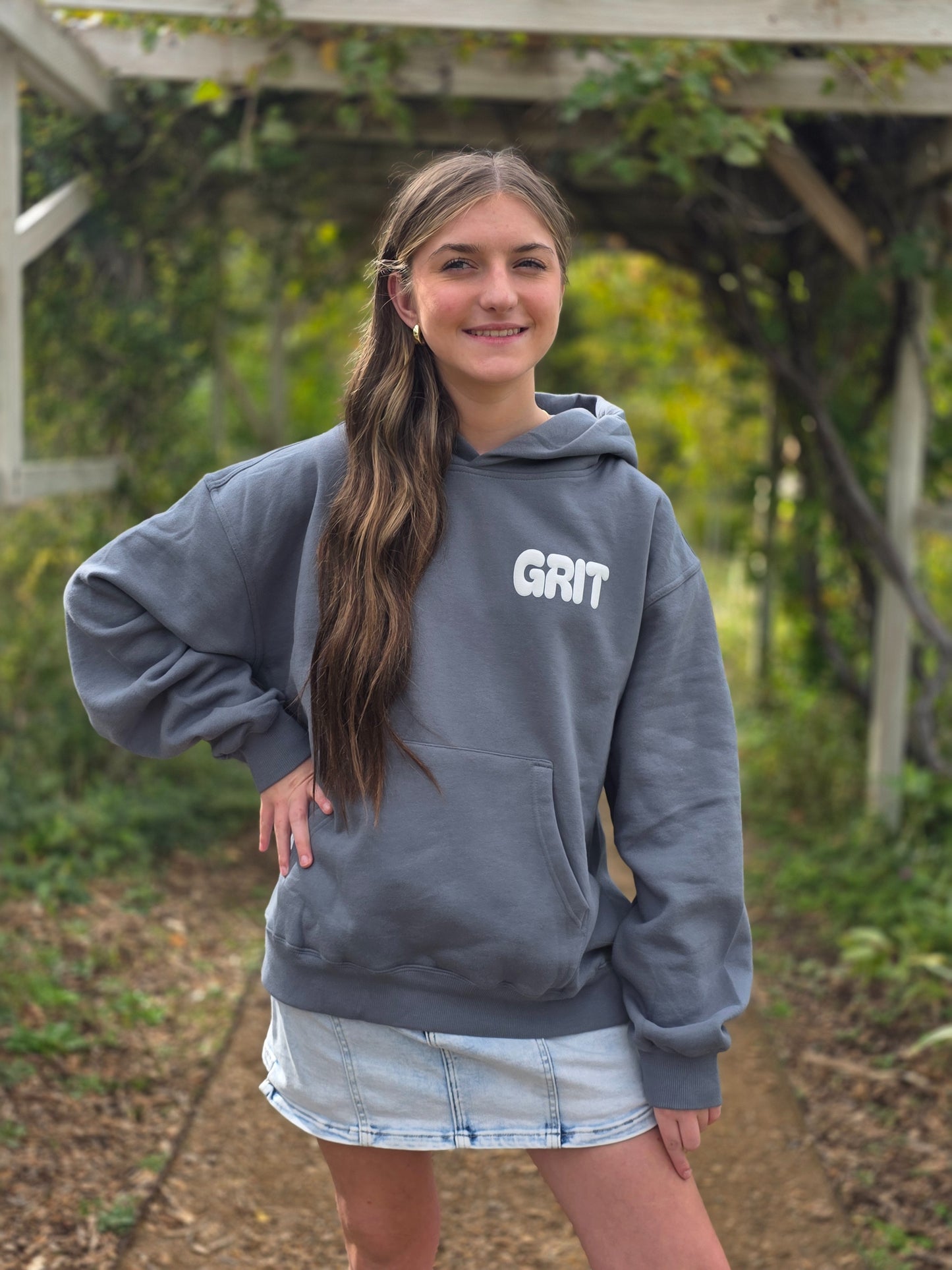 Person wearing a gray hoodie with 'GRIT' text, standing outdoors.