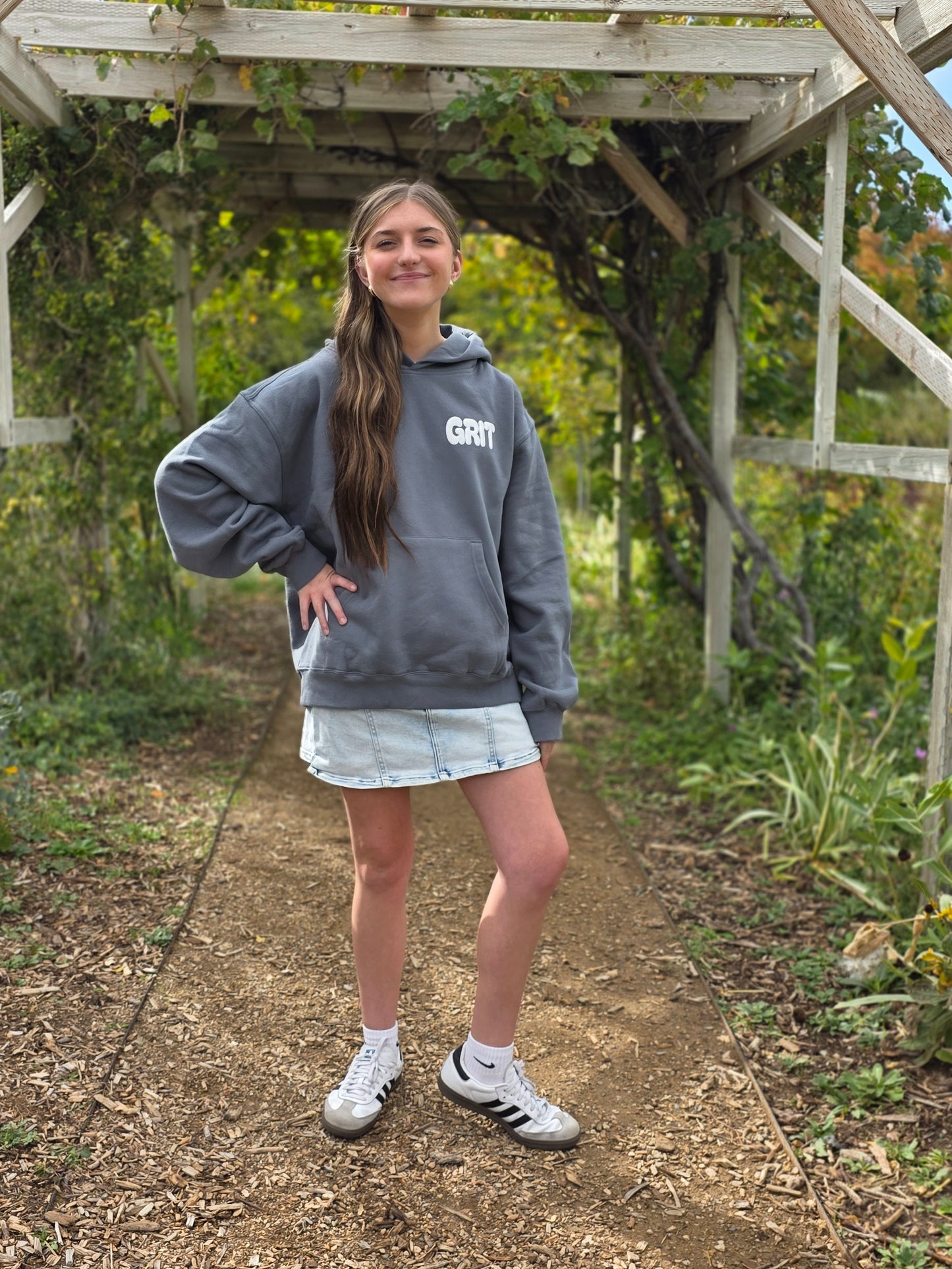 Person wearing a gray hoodie with 'GRIT' text, standing outdoors under a wooden structure.