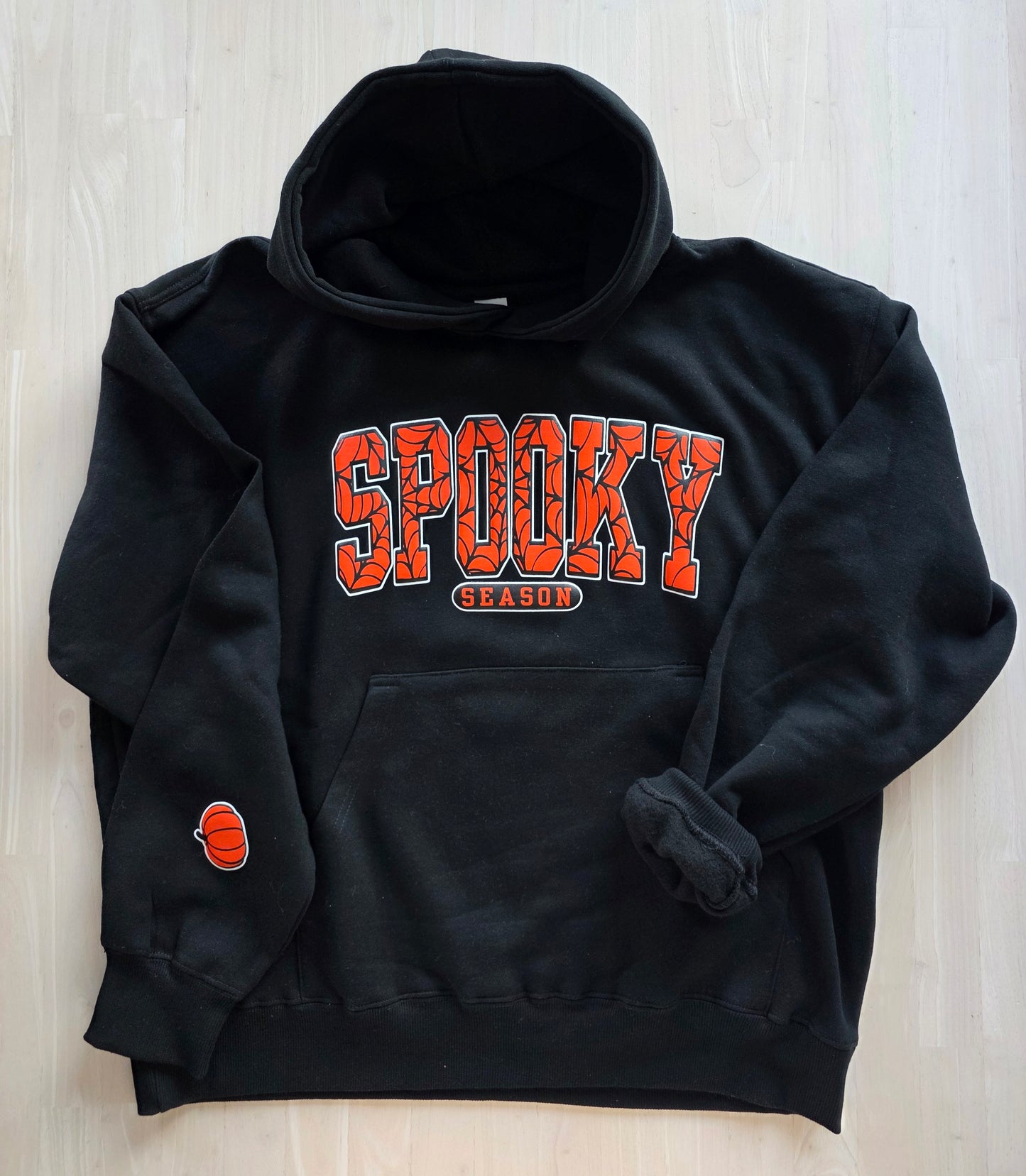 Black hoodie with 'Spooky Season' text on a light wooden surface