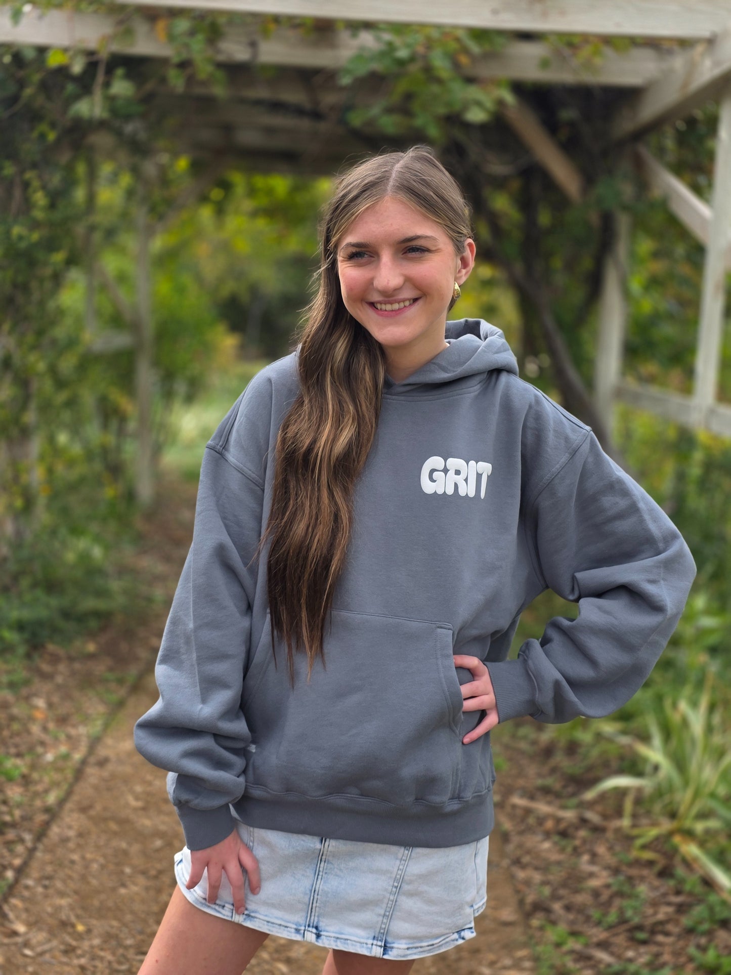 Person wearing a gray hoodie with 'GRIT' text, standing outdoors.