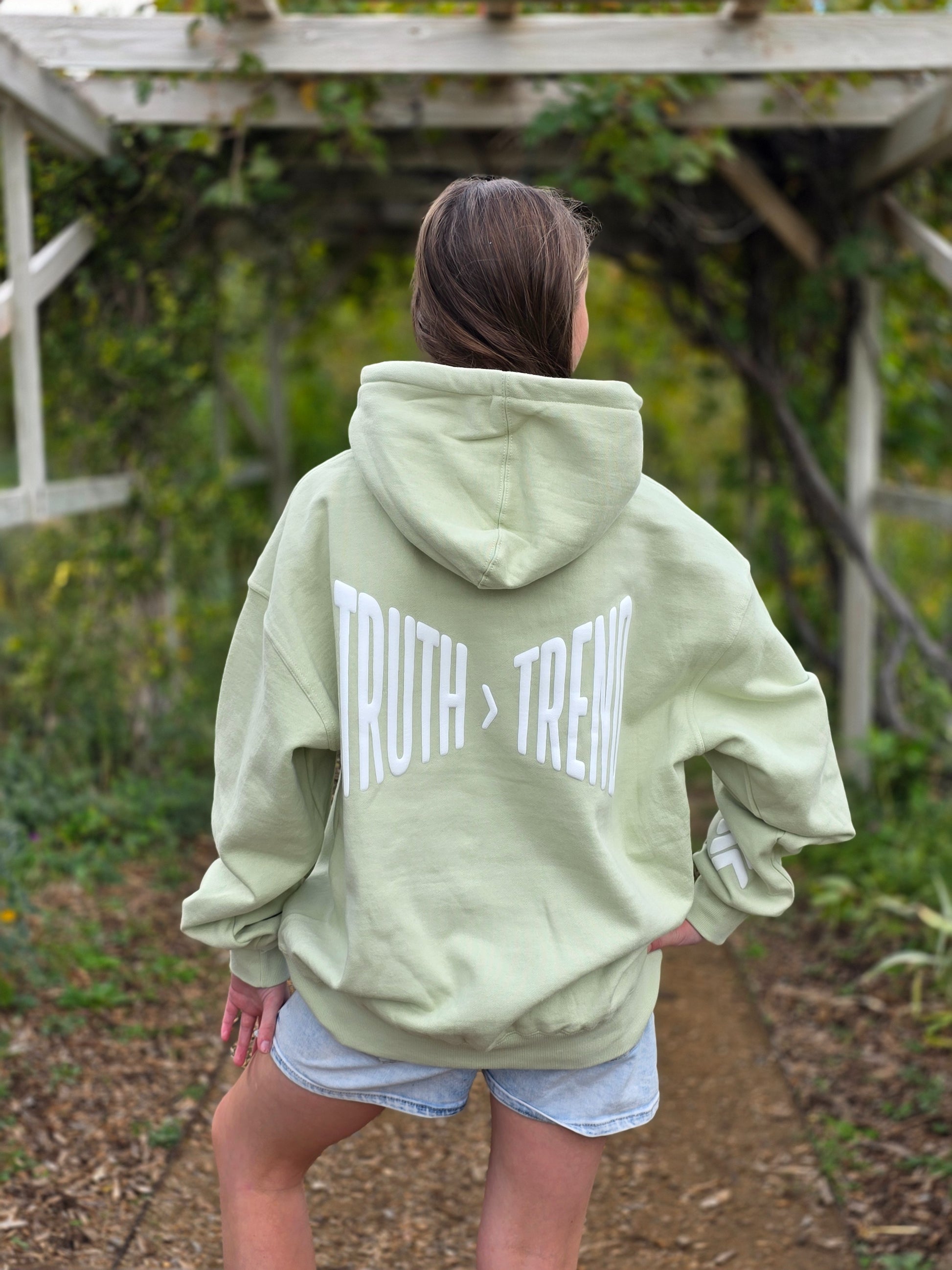 Person wearing a light green hoodie with 'TRUTH > TREND' text outdoors.