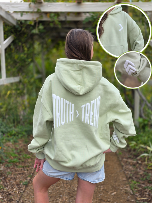 Person wearing a light green hoodie with 'TRUTH > TREND' text outdoors.