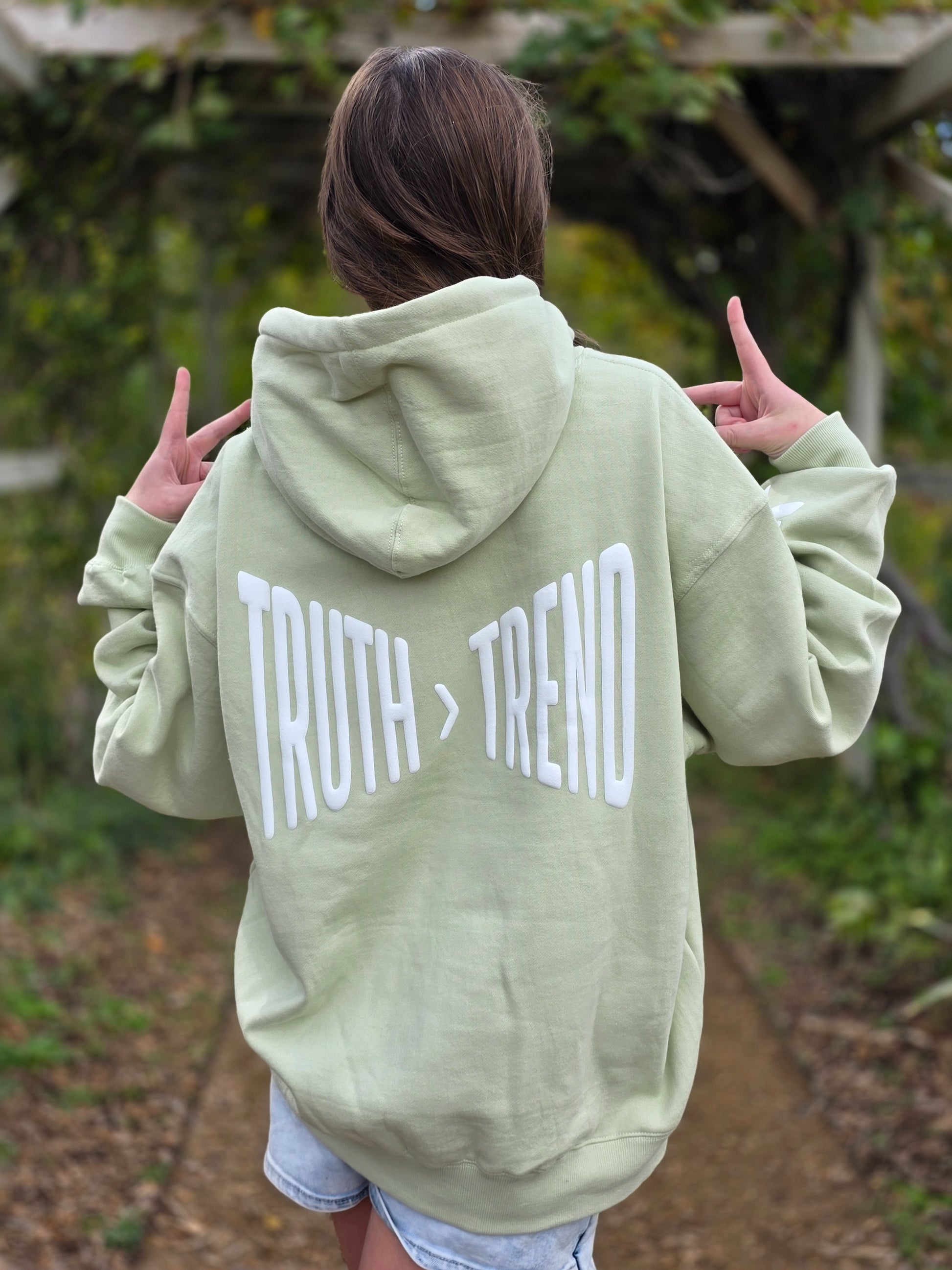 Person wearing a light green hoodie with 'TRUTH > TREND' text on the back, standing outdoors.
