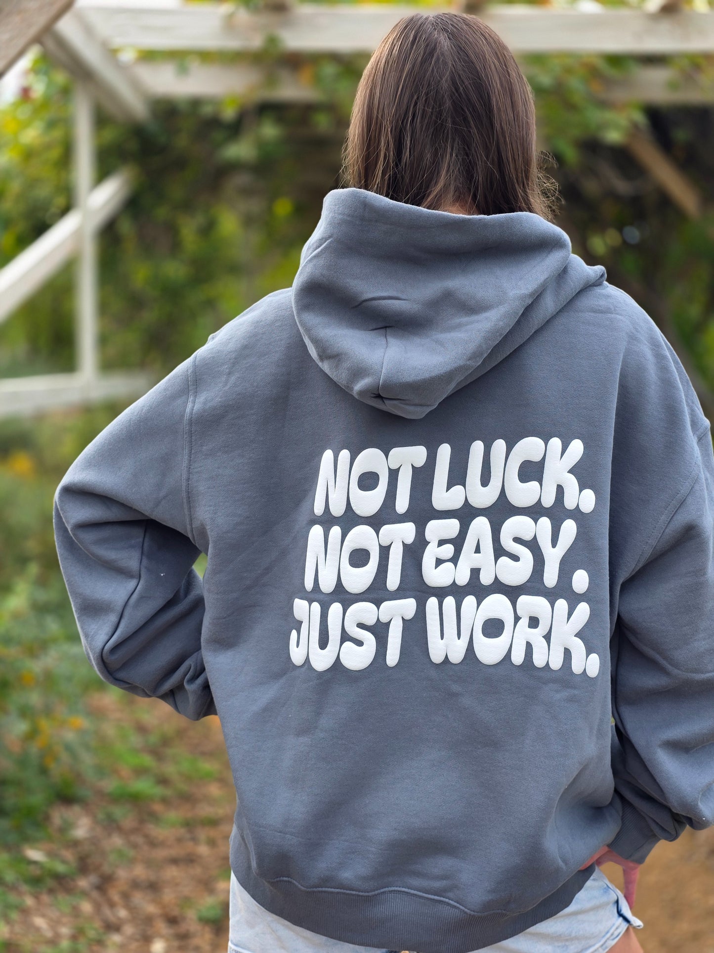 Person wearing a gray hoodie with motivational text on the back, standing outdoors.