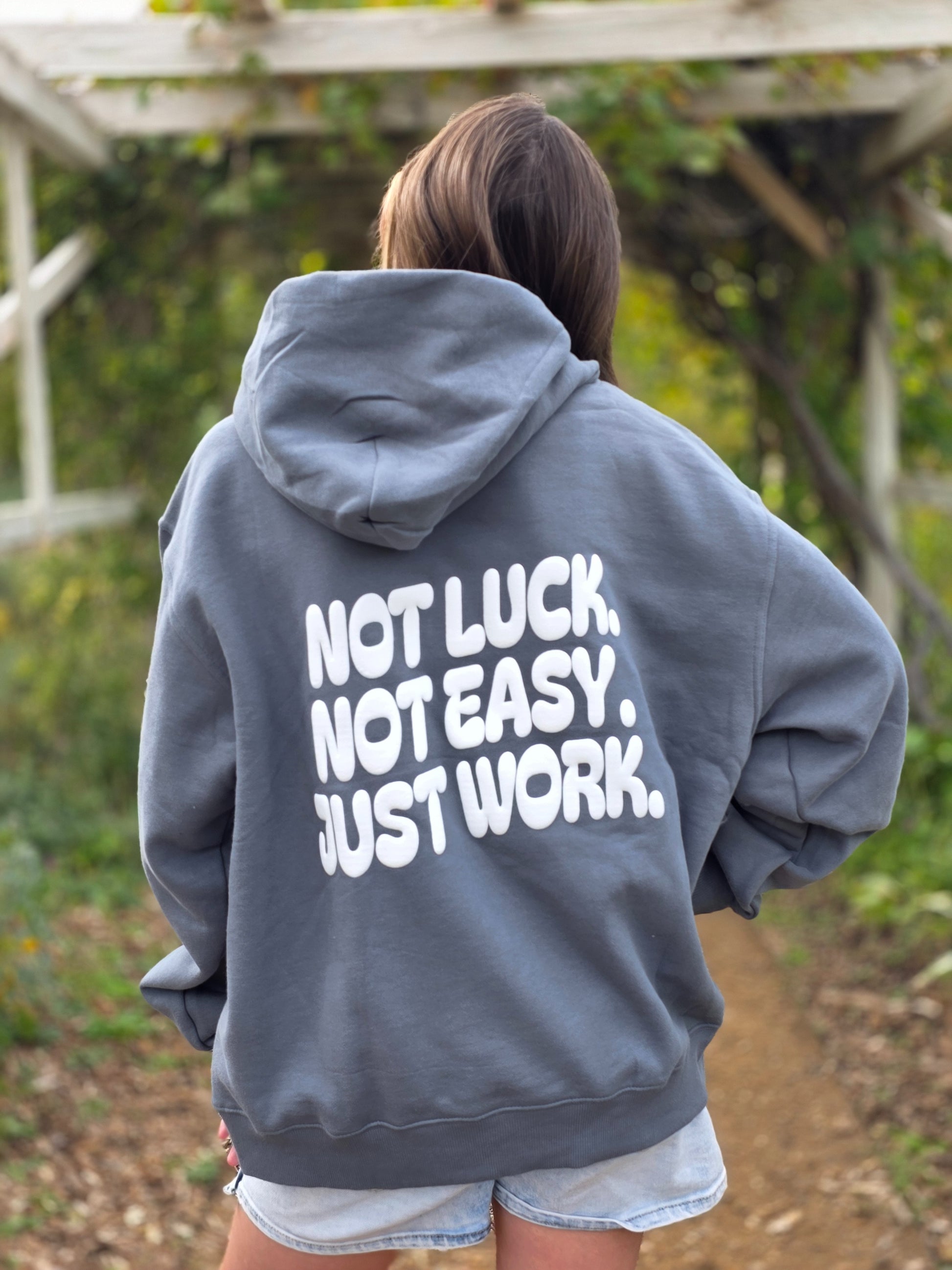 Person wearing a gray hoodie with motivational text on the back, standing outdoors.