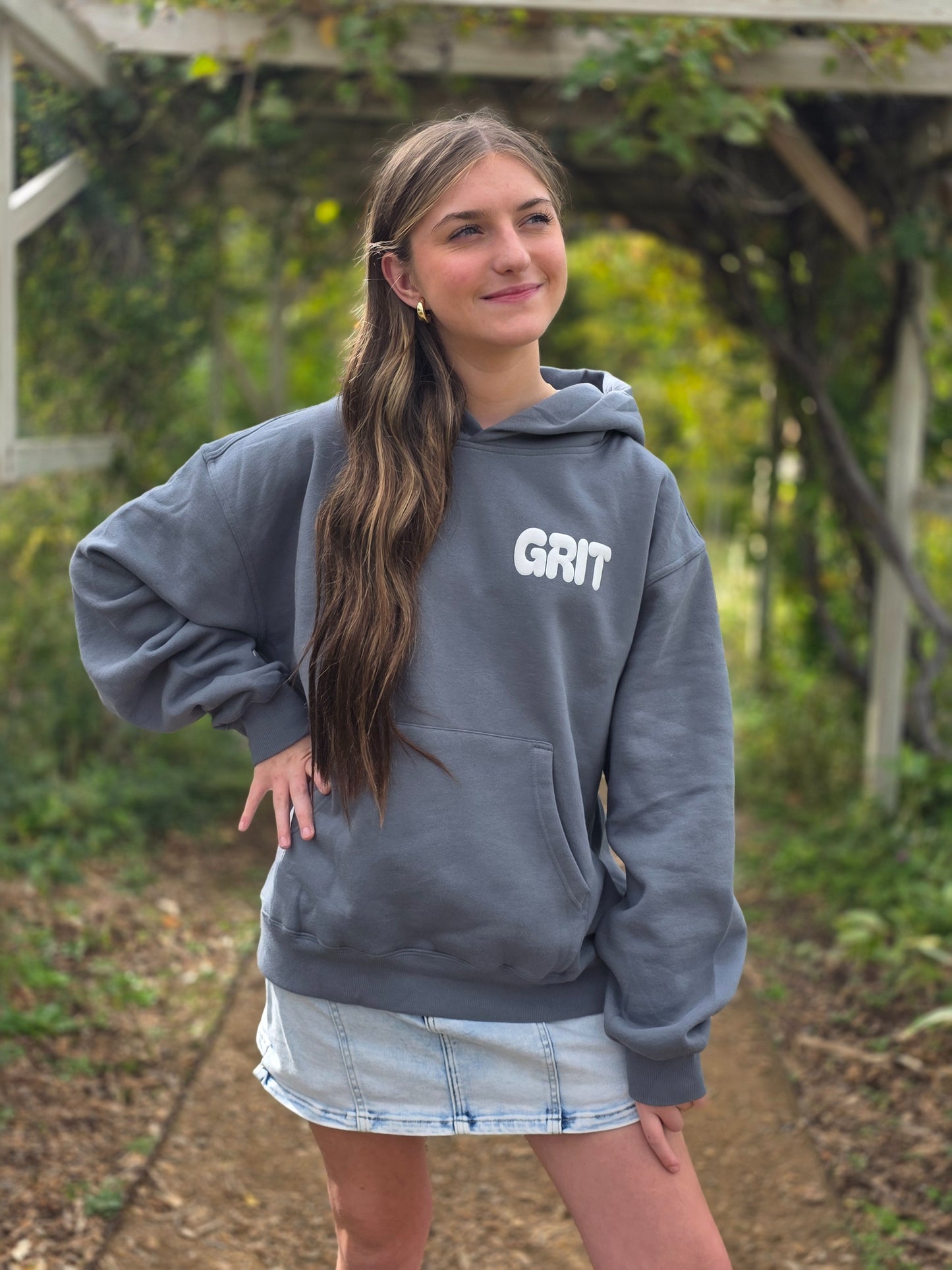 Woman wearing a gray hoodie with 'GRIT' text outdoors