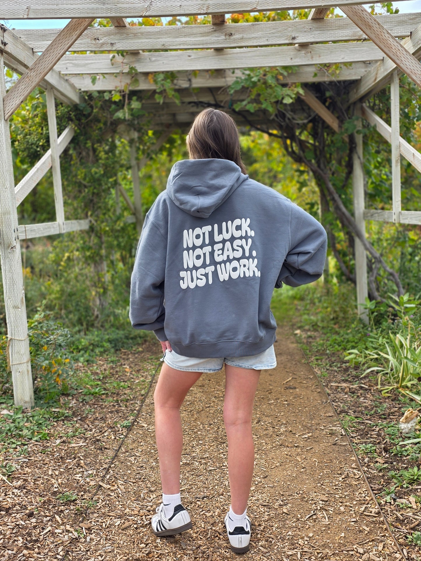 Person wearing a hoodie with 'Not Luck, Not Easy, Just Work' text outdoors.