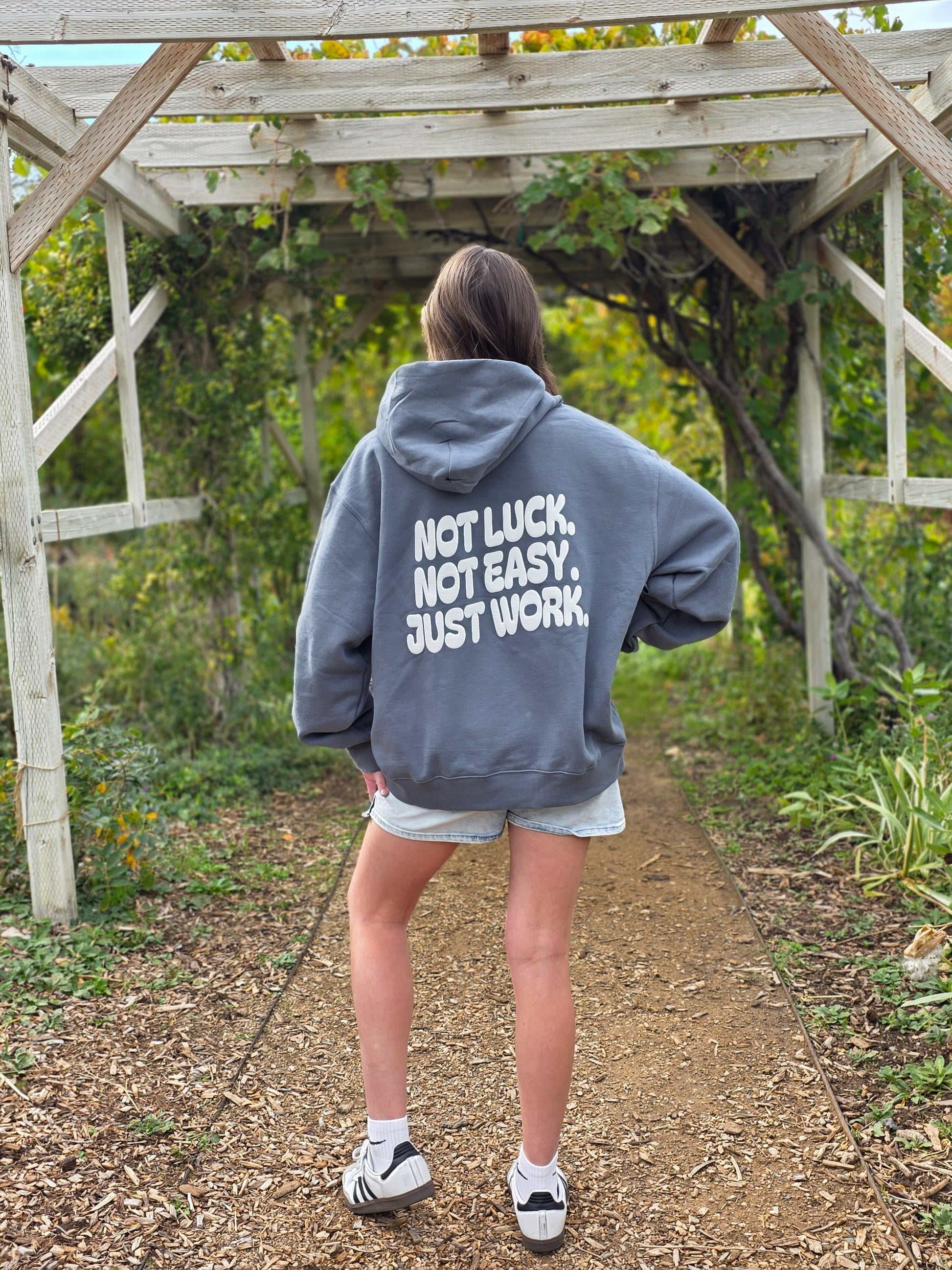 Person wearing a hoodie with 'Not Luck, Not Easy, Just Work' text outdoors.