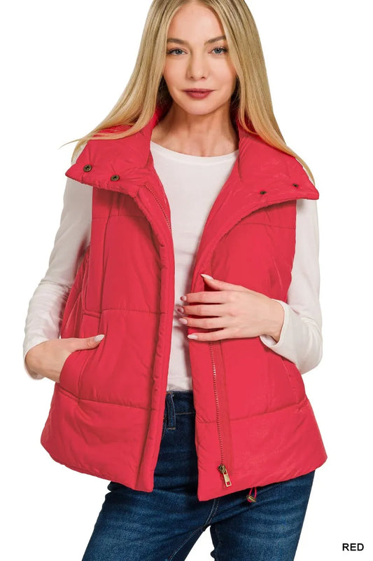 Woman wearing a red puffer vest over a white shirt and blue jeans on a white background